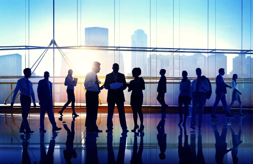 Silhouettes of business people collaborating in front of tall windows