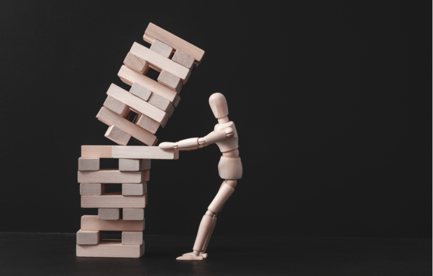 Wooden art doll pulling a Jenga tower onto itself